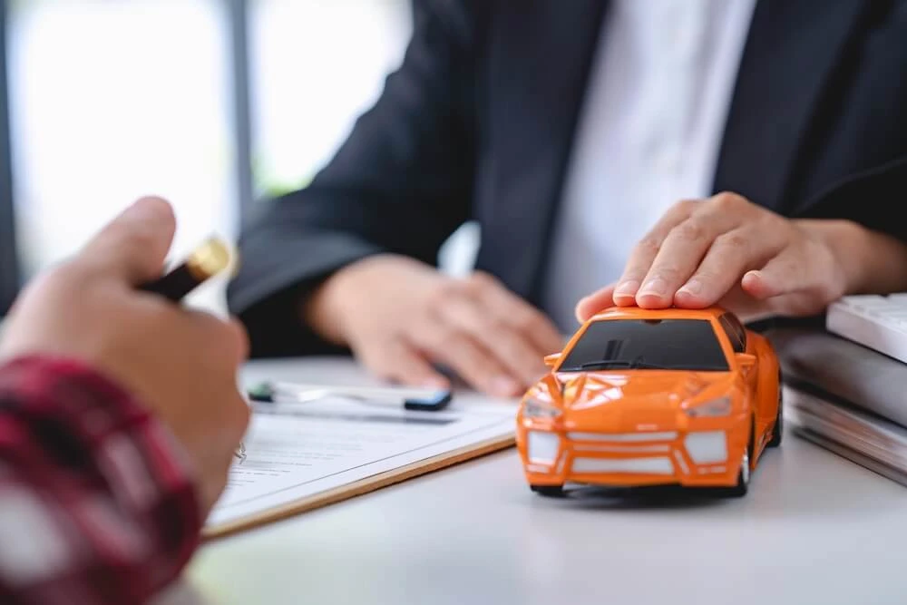 Imagen de unas manos protegiendo un Opel Astra de juguete de color naranja.